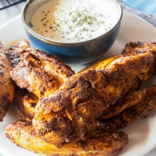 A plate of popeyes blackened chicken tenders with a small bowl of white dipping sauce.