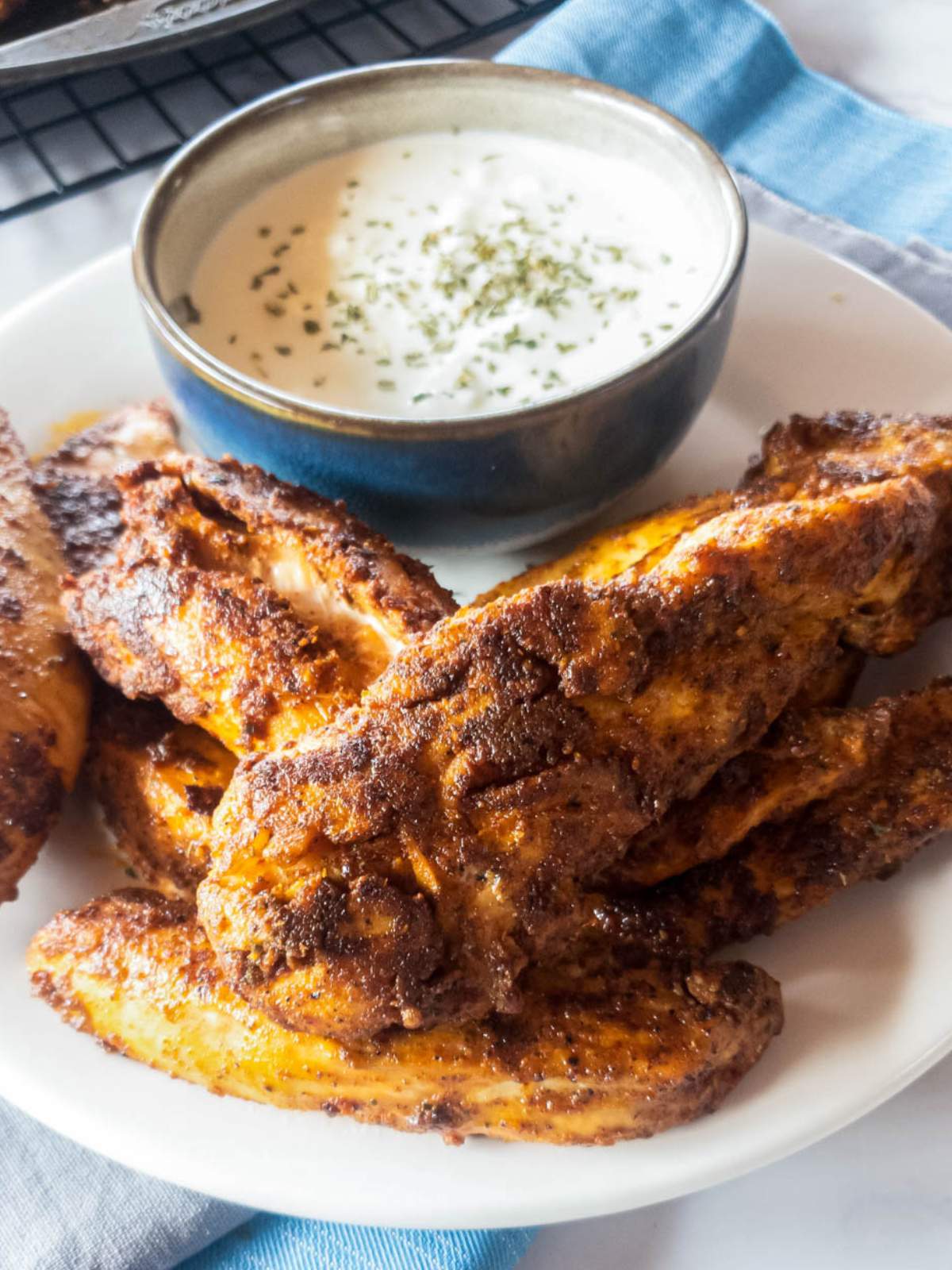 A plate of popeyes blackened chicken tenders with a small bowl of white dipping sauce.