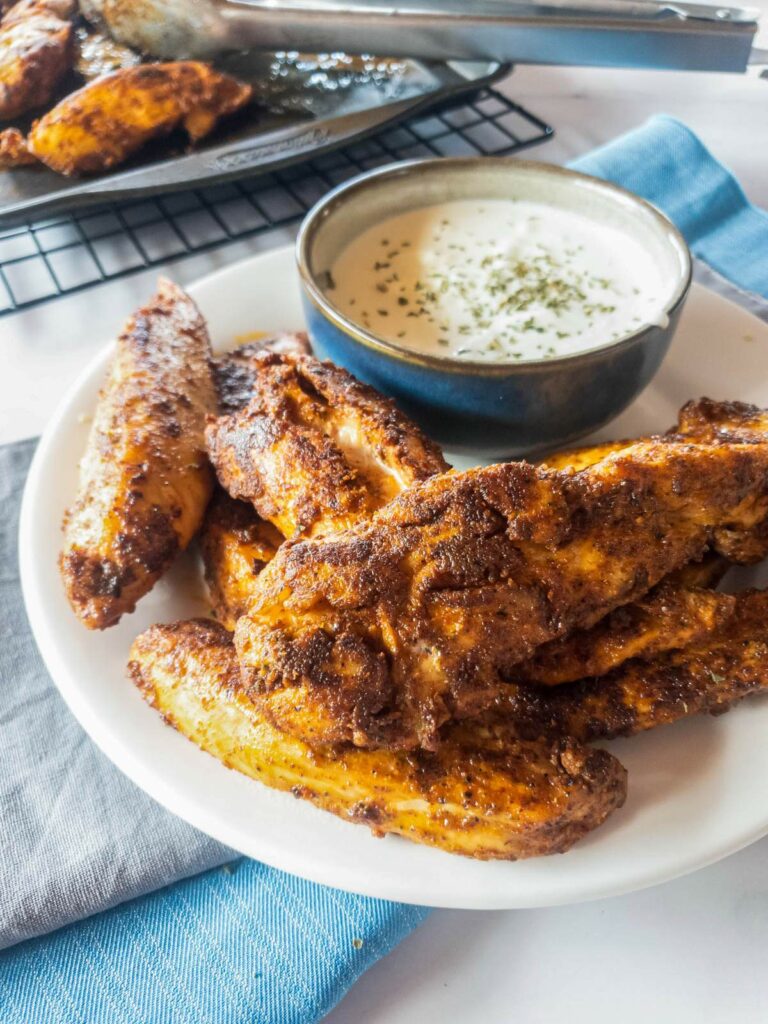 A plate of popeyes blackened chicken tenders is served with a bowl of creamy dipping sauce.