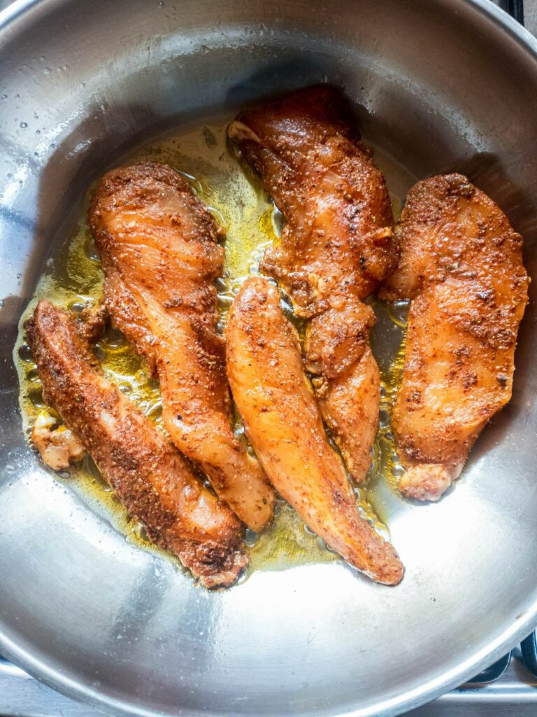 Cooking popeyes blackened chicken tenders in a stainless steel pan with oil.