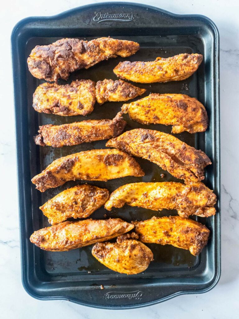 A baking tray with twelve popeyes blackened chicken tenders arranged in two rows.