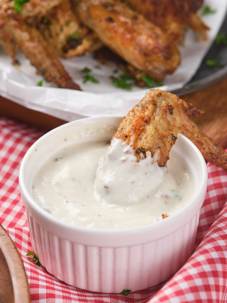 A chicken wing is partially dipped into a wingstop ranch dressing.