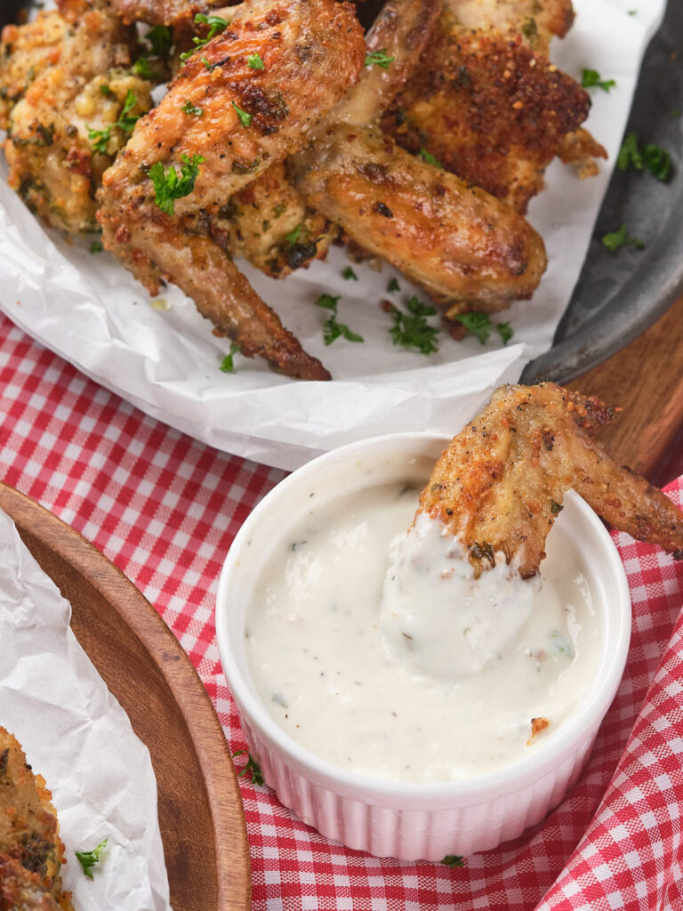 A chicken wing being dipped into a small white bowl of wingstop ranch dressing.