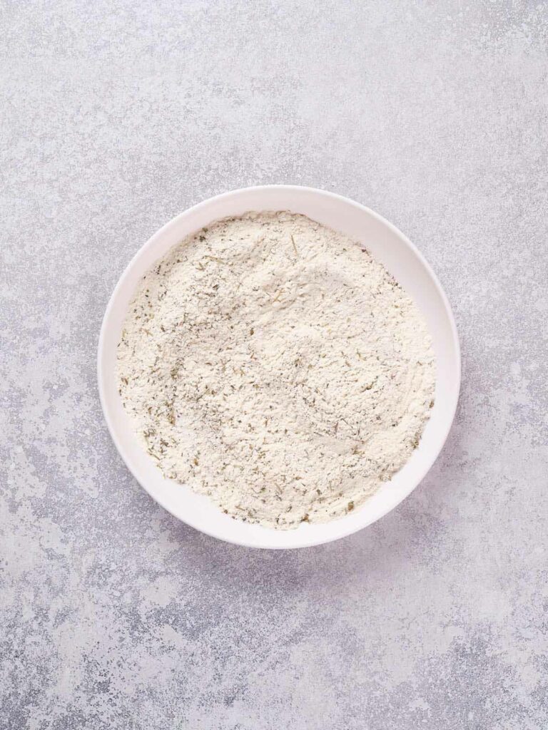 A white ceramic bowl filled with dry ingredients, placed on a textured, pale grey surface.