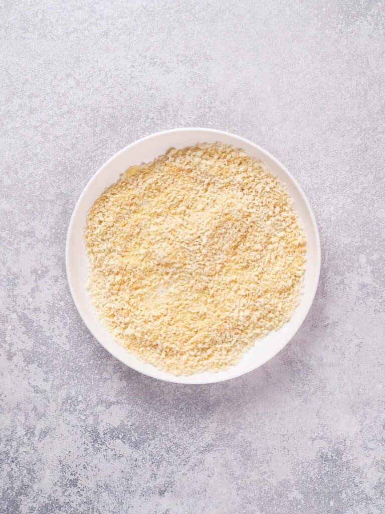 A round white bowl filled with breadcrumbs on a light textured surface.