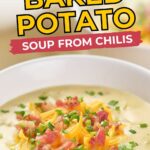 A bowl of baked potato soup topped with shredded cheese, bacon bits, and chopped chives.