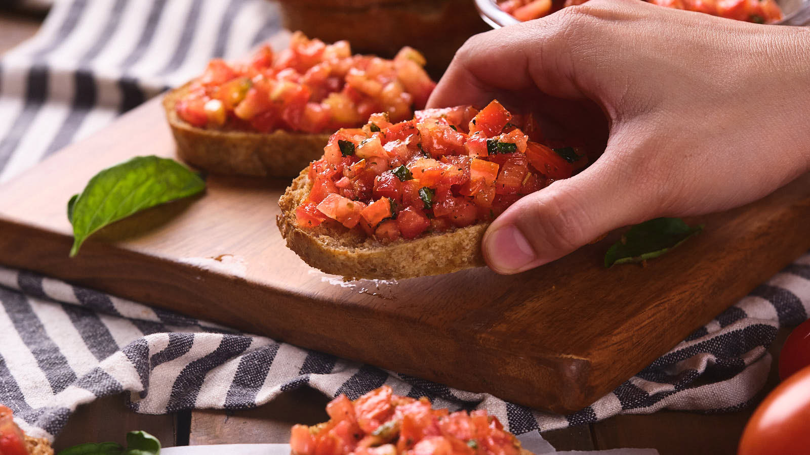 A person's hand picking up a slice of bruschetta al pomodoro.