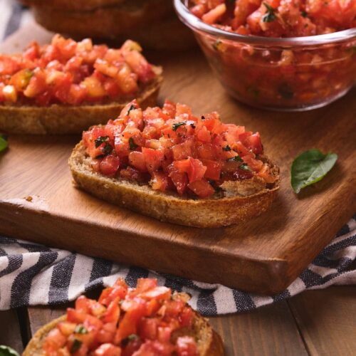 A wooden board holds several pieces of bruschetta al pomodoro.