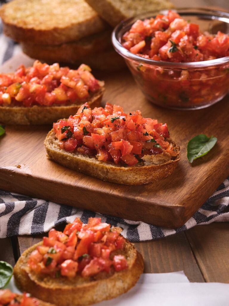 A wooden board holds several pieces of bruschetta al pomodoro.