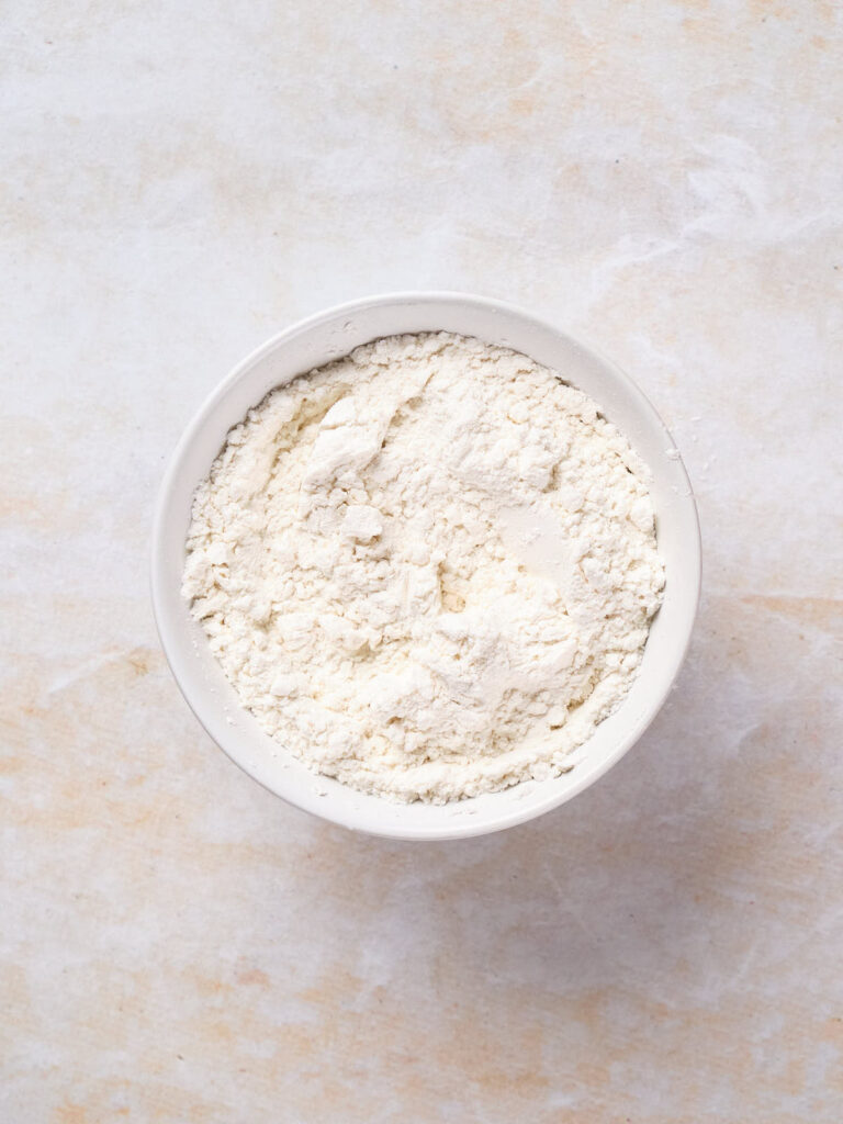 A white bowl filled with flour, placed on a light-colored surface.