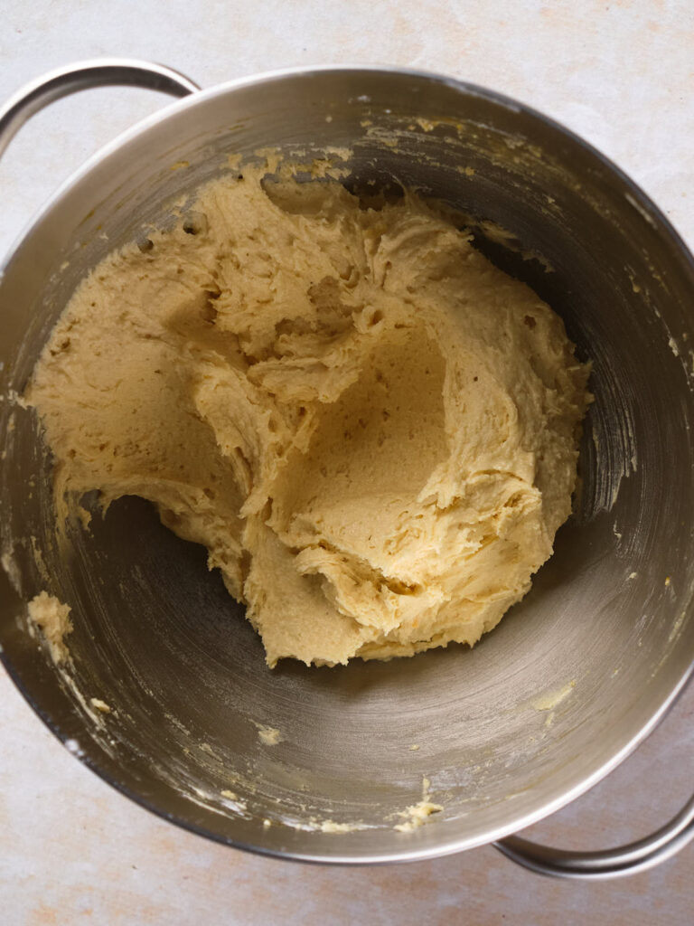 A stainless steel mixing bowl contains chocolate chip cookies batter or dough against a light background.