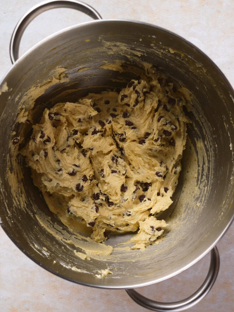 A metal mixing bowl filled with cookie dough mixed with chocolate chips.