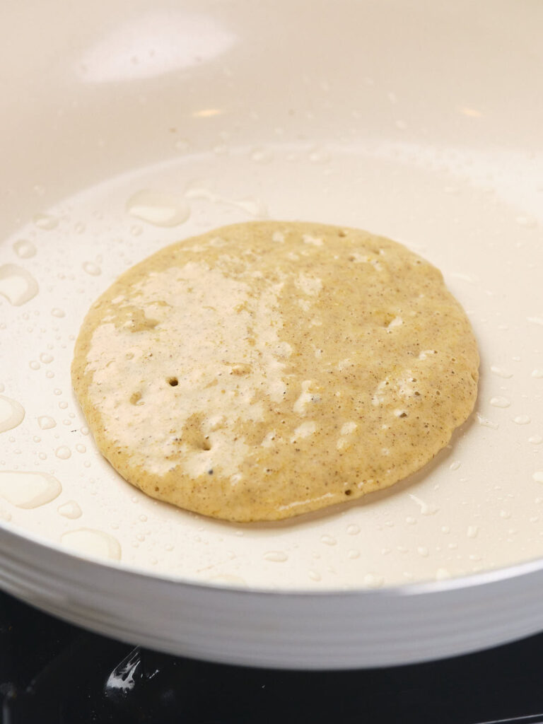 Close-up of pancake batter cooking in a lightly greased white non-stick frying pan.