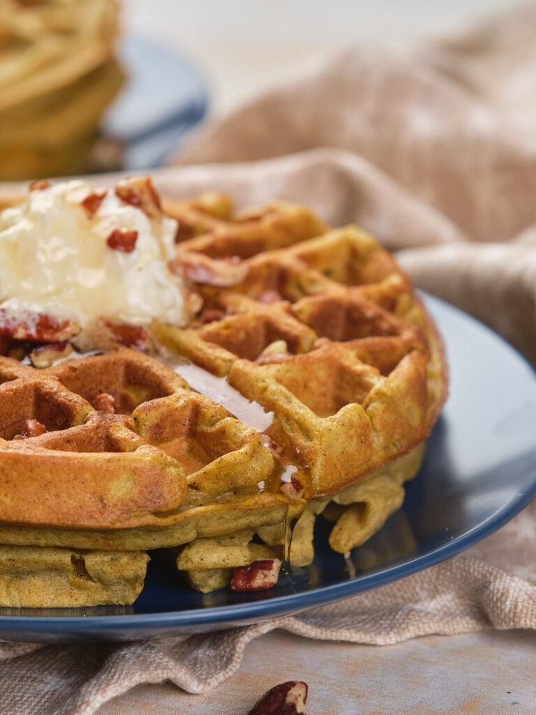 A close-up of a stack of pumpkin pecan waffles topped with a dollop of butter.