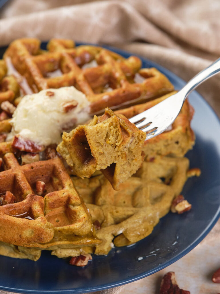 A fork holding a piece of waffle topped with syrup and pecans.