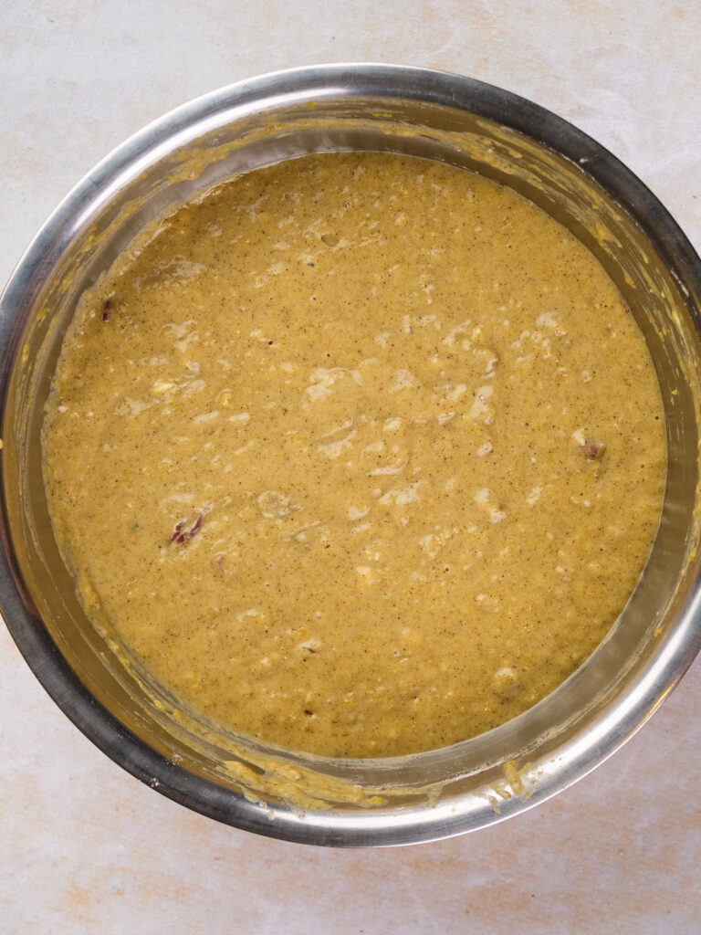 A large silver mixing bowl filled with thick, yellow batter mixed with visible chunks of ingredients.