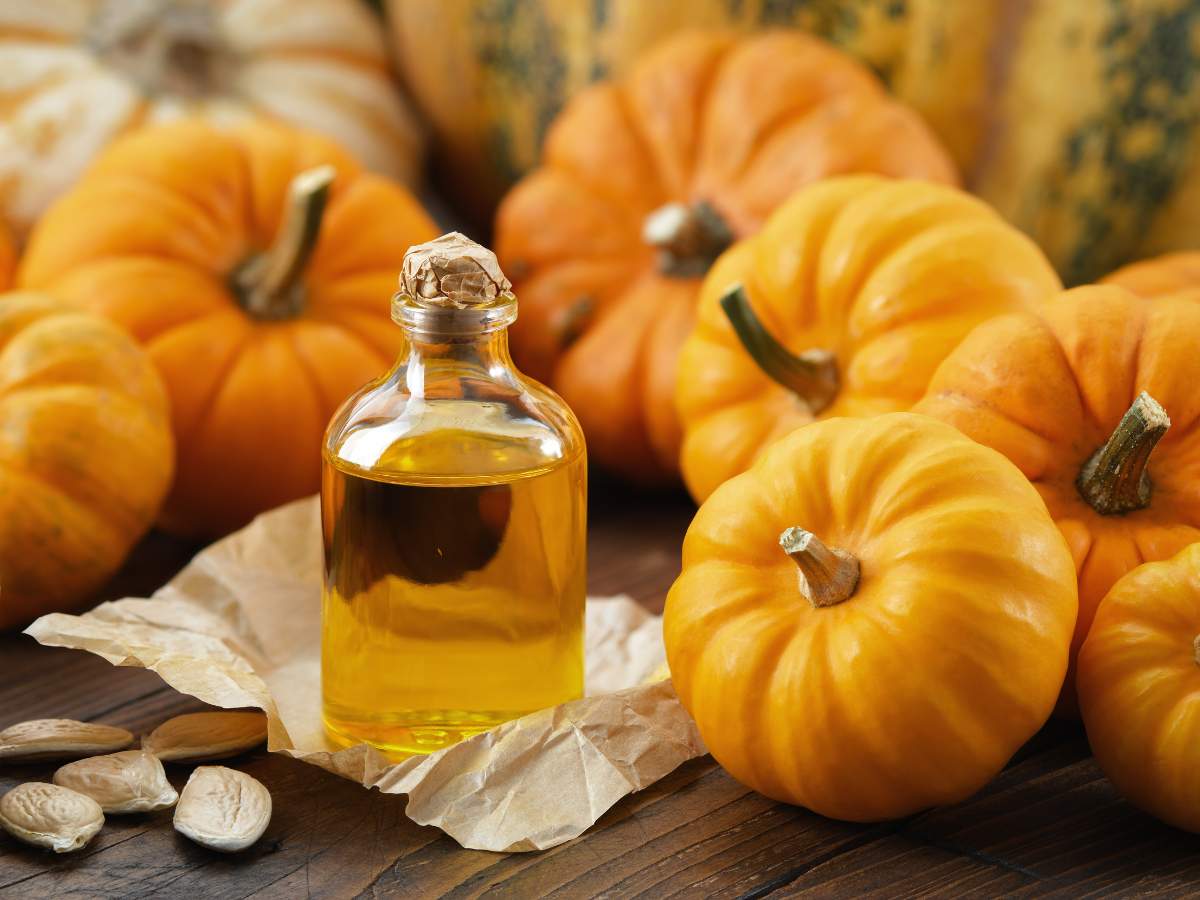 A small glass bottle filled with a golden liquid, surrounded by miniature pumpkins and pumpkin seeds.