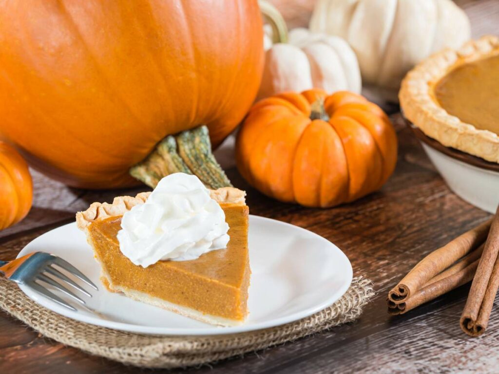 A slice of pumpkin pie topped with whipped cream on a white plate.