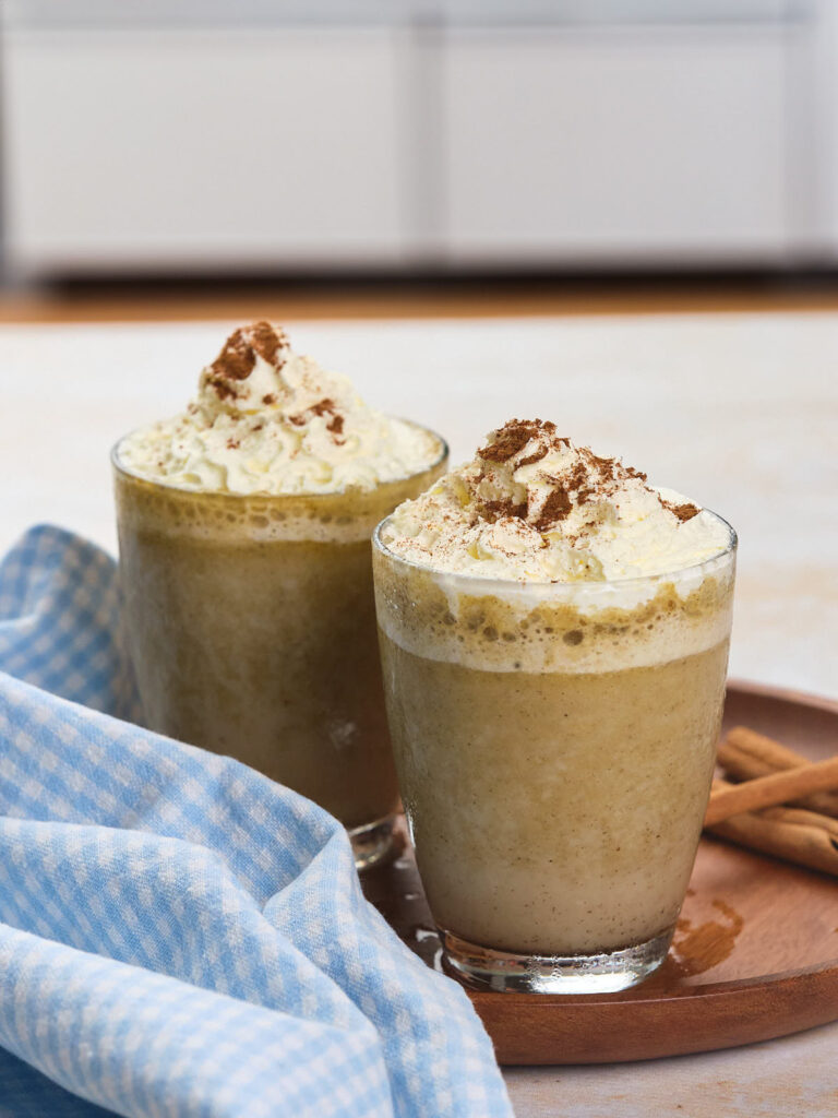 Two glass mugs filled with pumpkin spice frappuccino topped topped with whipped cream.