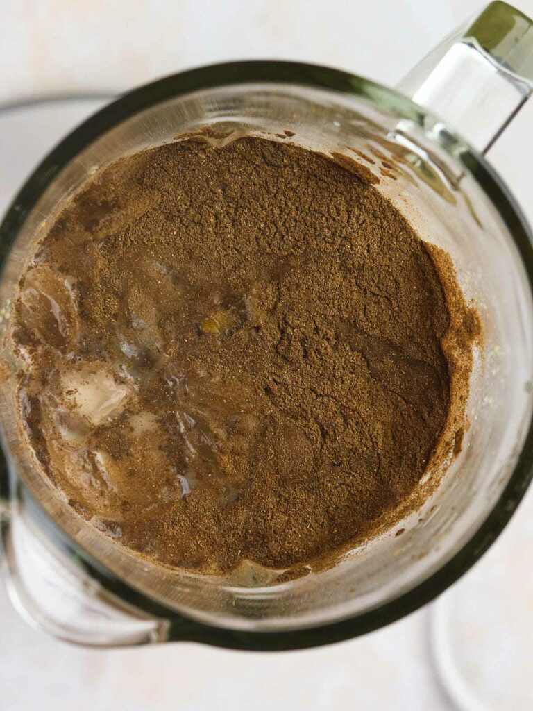 Top view of a blender filled with brown powdered ingredients and ice, partially blended.