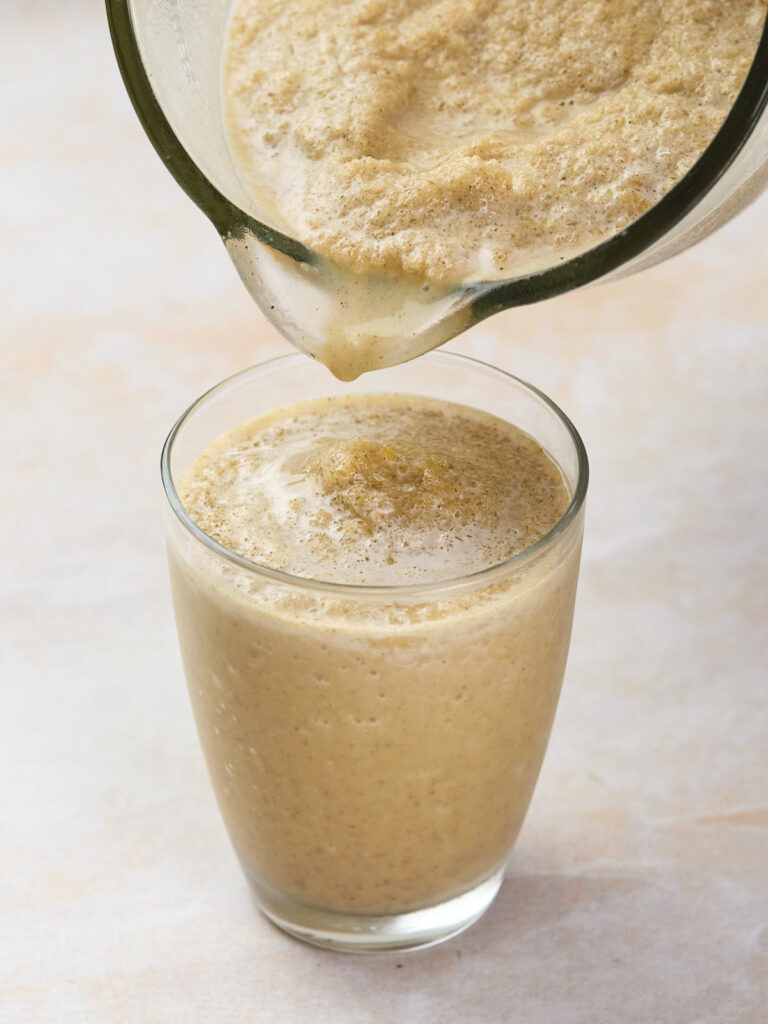 Thick, blended beverage being poured into a clear glass from a pitcher, showcasing a frothy texture.