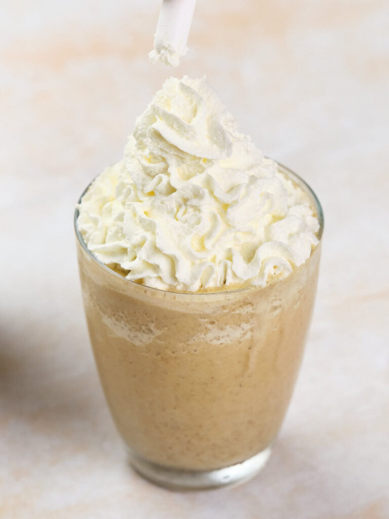 A glass filled with a blended coffee drink, topped with a generous amount of whipped cream and a straw.