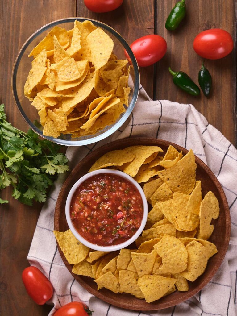 A bowl of tortilla chips and a smaller bowl of salsa ranchera are placed on a wooden table.