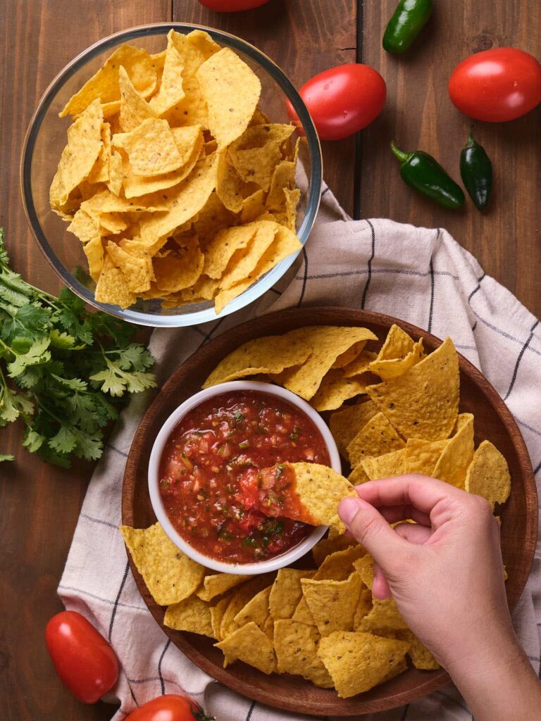 A hand is dipping a chip into salsa ranchera.