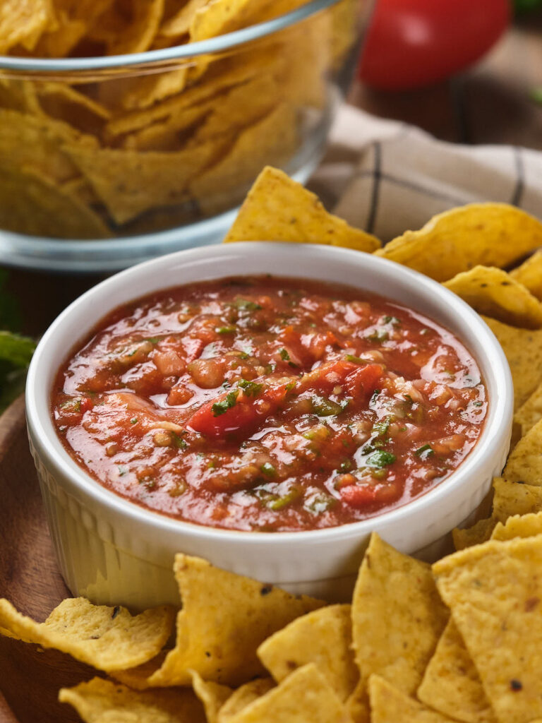 A bowl of salsa ranchera surrounded by tortilla chips on a wooden surface.