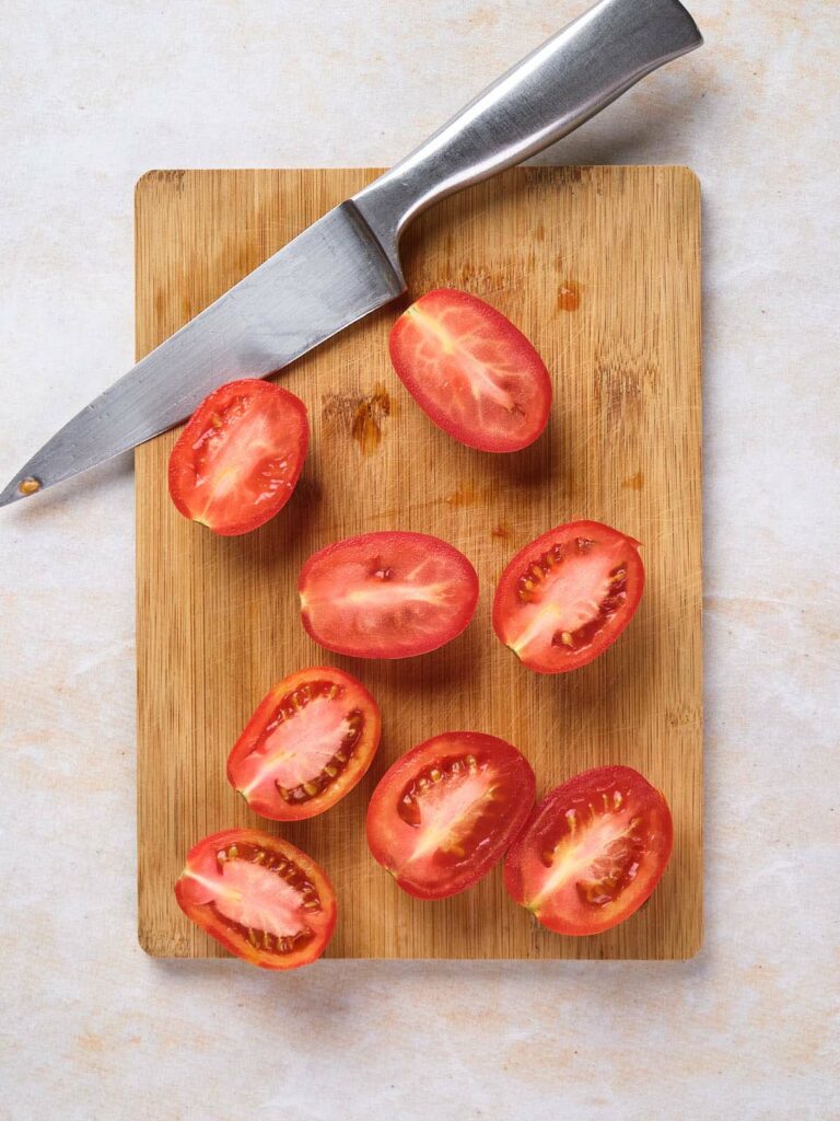 A wooden cutting board with eight halved tomatoes and a knife placed on top.