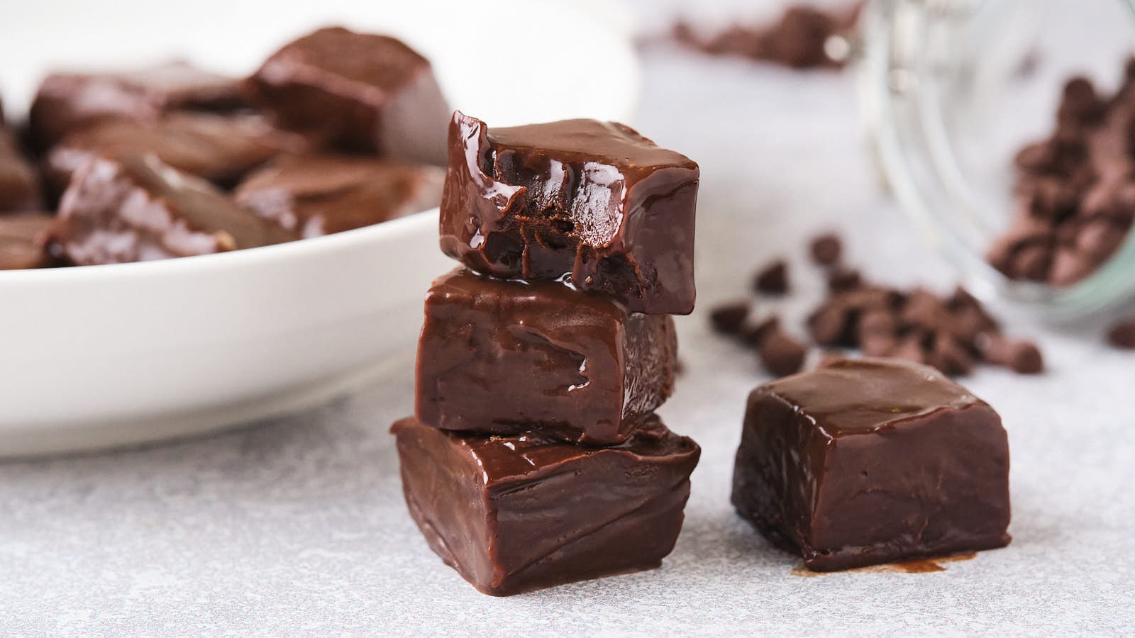 Close-up view of several pieces of chocolate fudge, with some stacked and one showing a bite taken out of it.