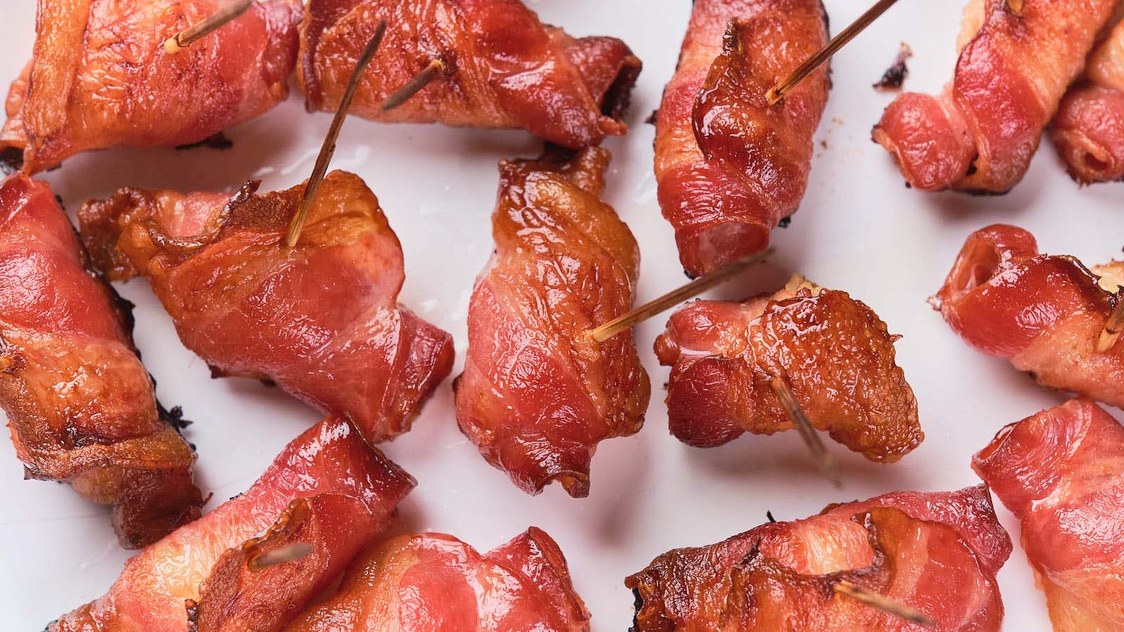 Close-up of several bacon-wrapped items secured with toothpicks, arranged on a white surface.