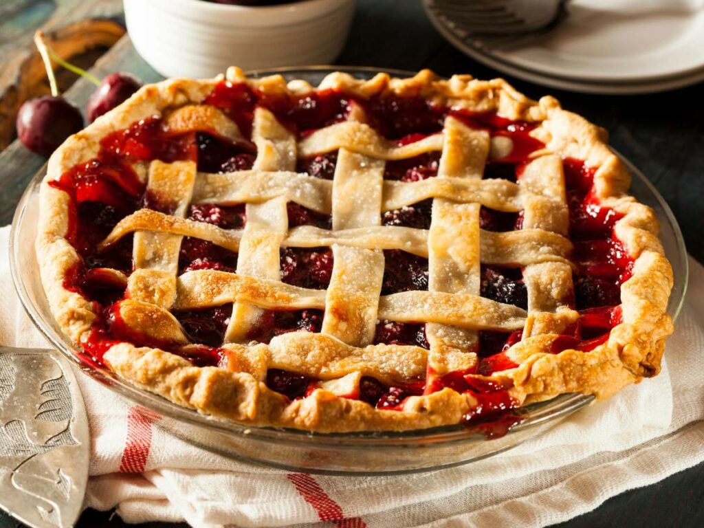 A cherry pie with a lattice crust sits on a white and red-striped cloth.