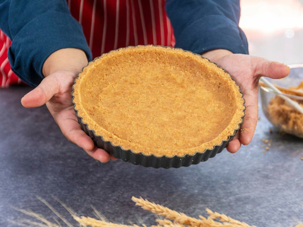 A person holds a round, unfilled pie crust in a black baking tin over a gray counter.