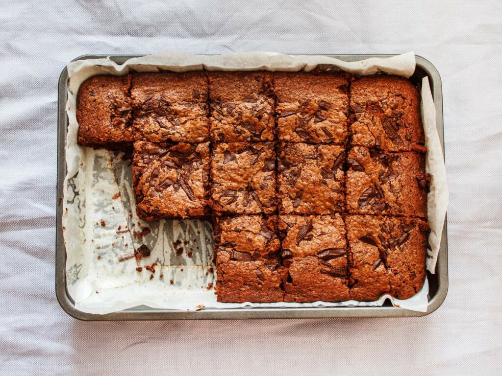 A tray of brownies, cut into squares, with a few pieces missing, on a white cloth background.