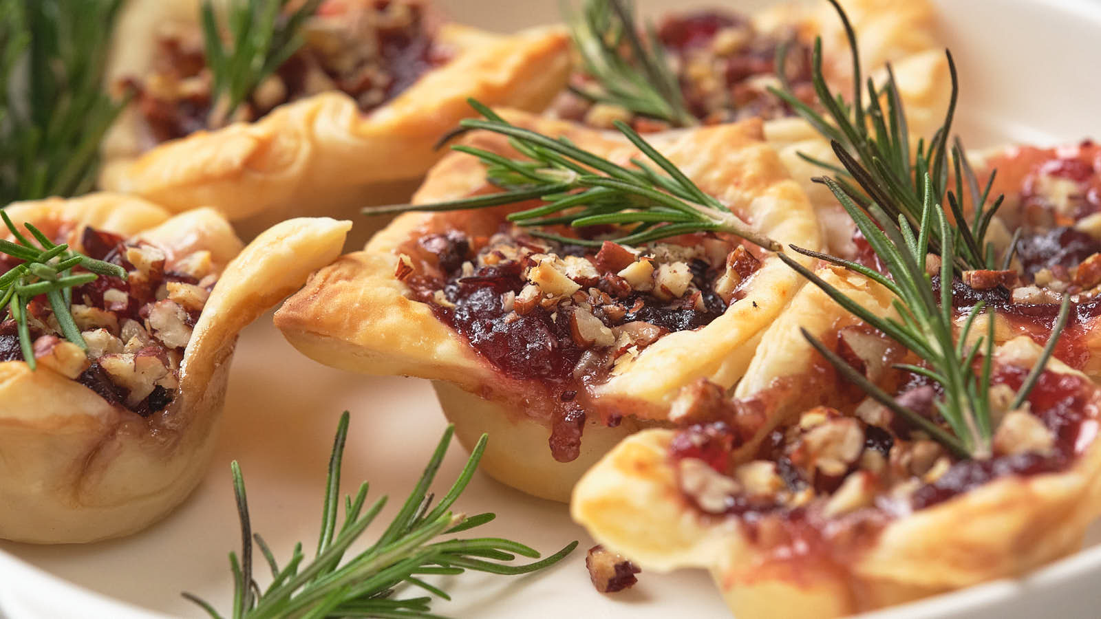 Brie bites filled with jam and chopped nuts, topped with rosemary sprigs, on a white plate.