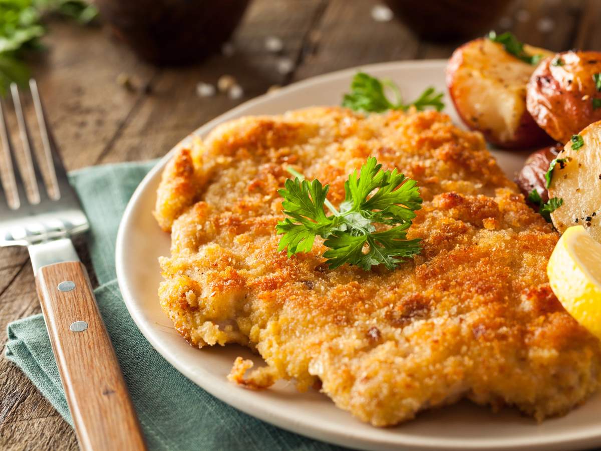 A breaded chicken cutlet garnished with parsley, served with roasted potatoes and a lemon wedge.