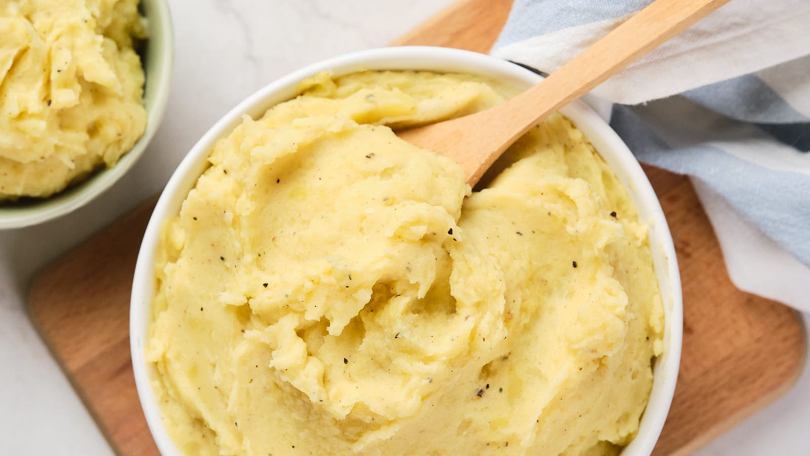 A bowl of garlic mashed potatoes with a wooden spoon resting on top.