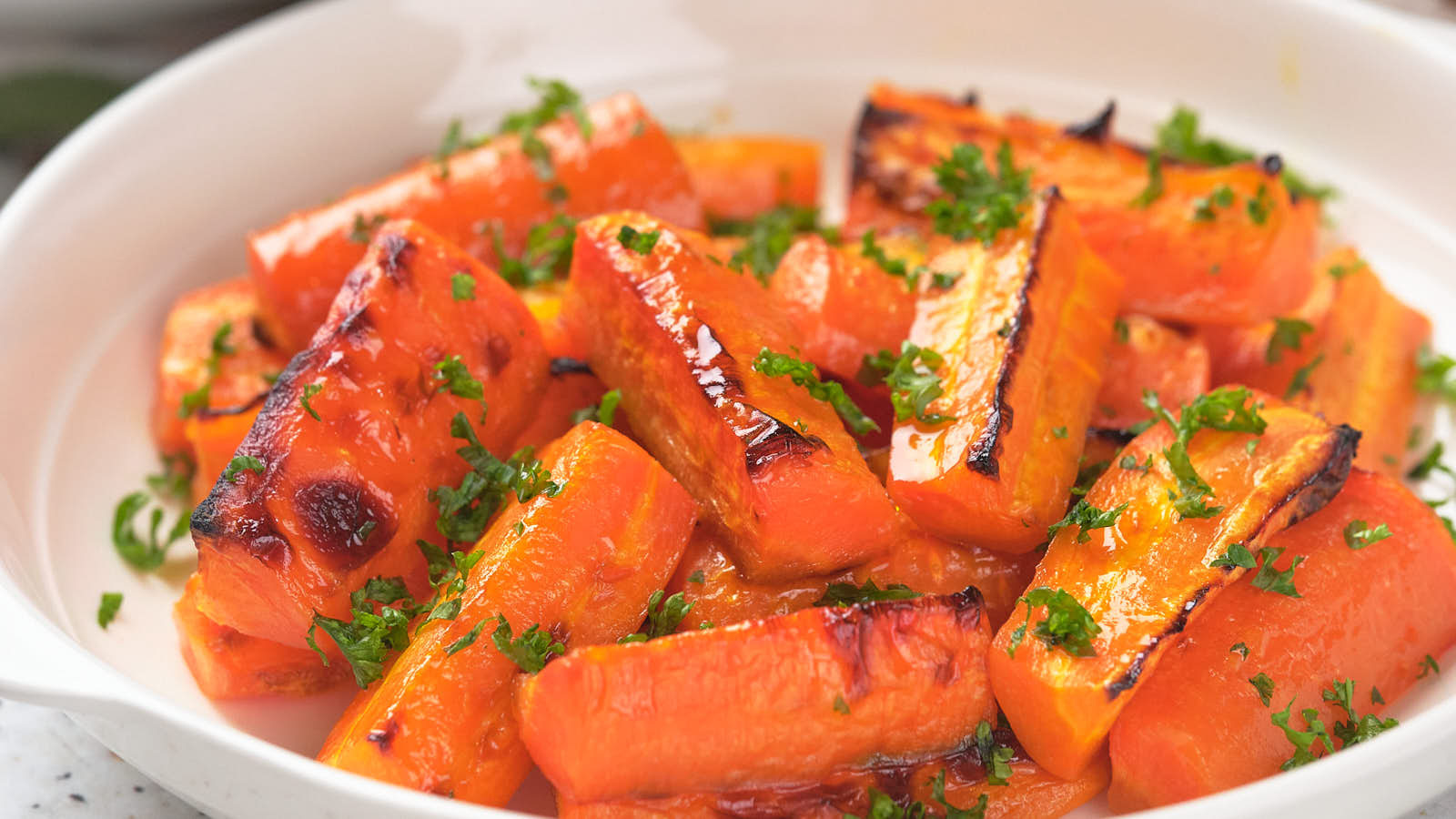 Honey glazed carrots in a white dish, garnished with chopped parsley.