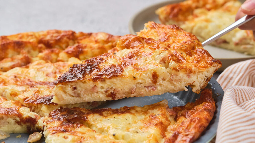 A slice of impossible quiche being lifted from a whole quiche on a plate.