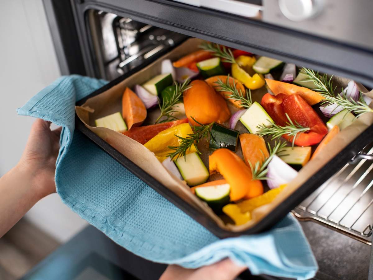 A baking tray containing vegetables being put into the oven.