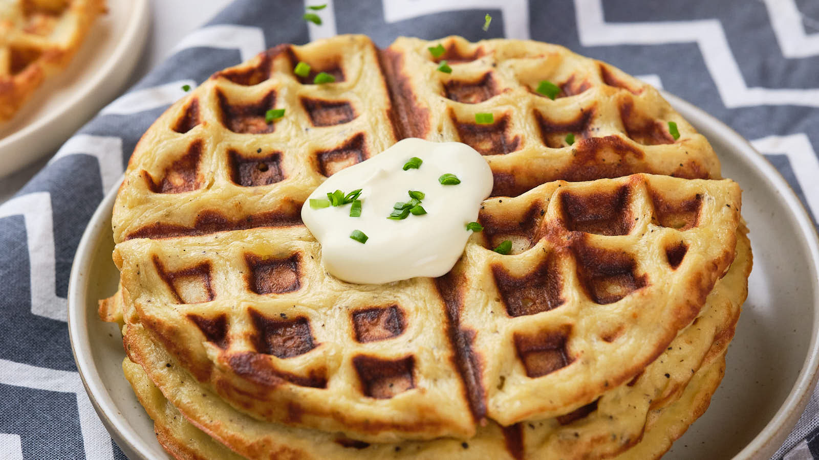 A stack of round, golden-brown potato waffles topped with a dollop of cream.