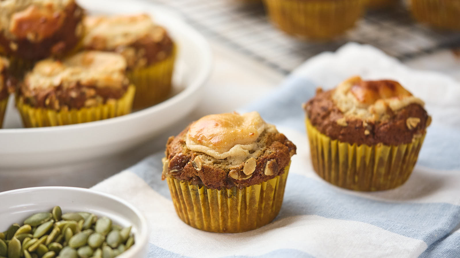 Two pumpkin and cream cheese muffins sit on a blue and white cloth.