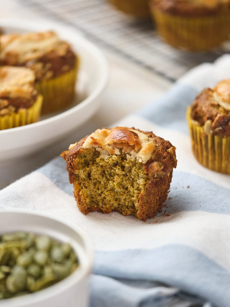 A close-up of a partially-eaten pumpkin and cream cheese muffins with a crumbly texture.