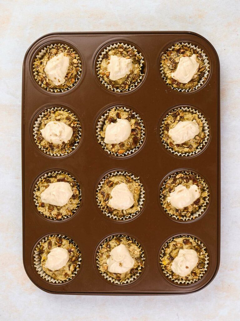 A muffin tray with twelve paper liners, each filled with a mixture of pumpkin and cream cheese muffin batter.