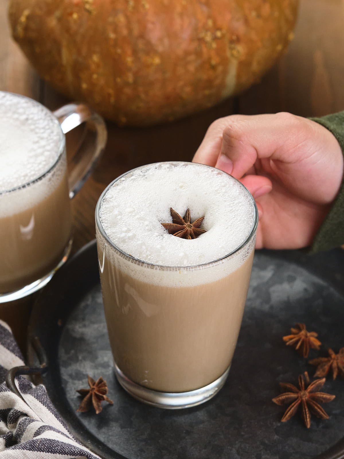 A hand holds a frothy pumpkin spice chai latte topped with a star anise.