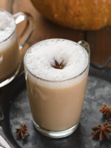 Clear glass mug filled with frothy pumpkin spice chai latte, placed on a dark tray with additional star anise pieces scattered around.