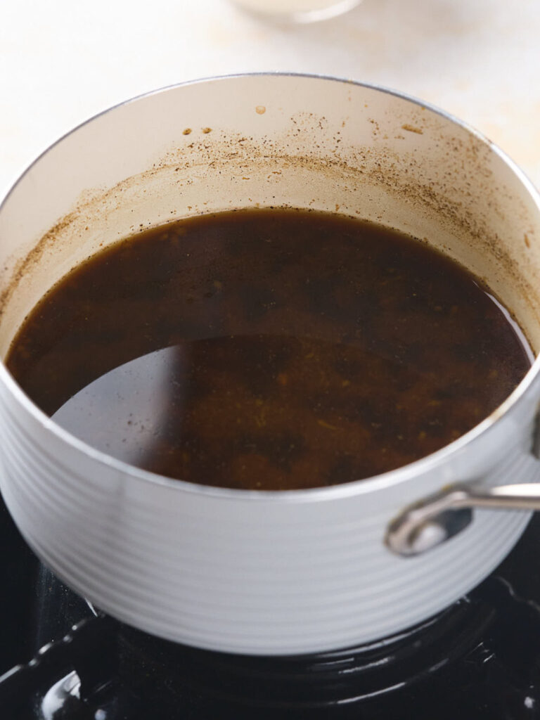 A white pot containing a dark, simmering liquid on a stovetop.