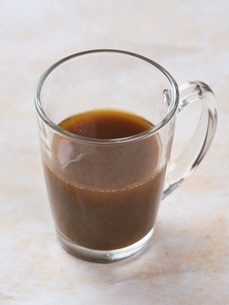 A clear glass mug filled with a dark brown liquid on a light surface.