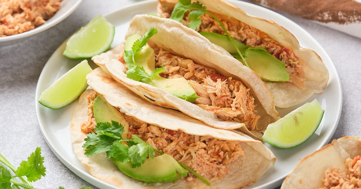 Three salsa chicken tacos with avocado slices, cilantro, and lime wedges on a white plate.